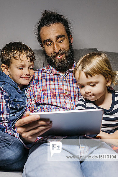 Portrait of father sitting on the couch with his children watching movies on digital tablet