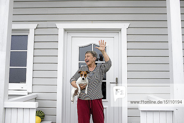 Glückliche ältere Frau auf der Veranda mit ihrem Hund  der ihre Hand hebt