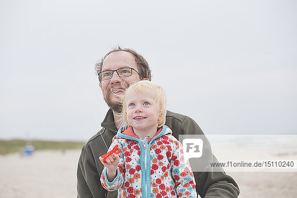Vater und kleine Tochter spielen mit dem Drachen am Strand