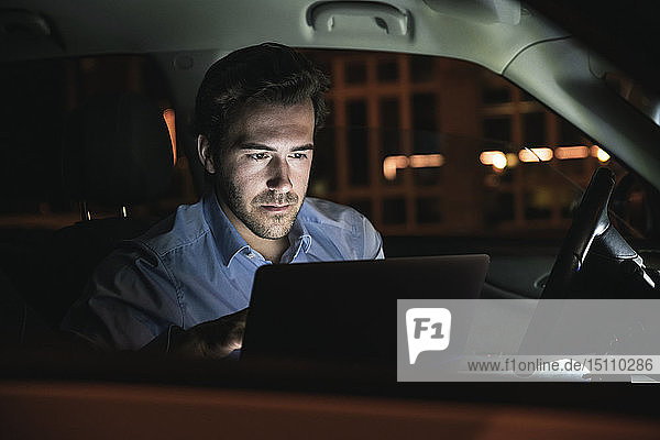 Young man using laptop in car at night