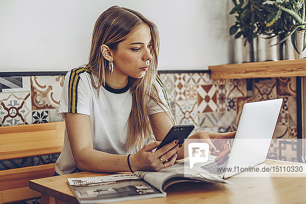Junge Frau benutzt Mobiltelefon und Laptop im Café