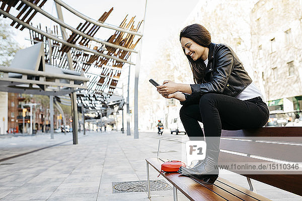 Junge Frau sitzt auf einer Bank und benutzt ein Smartphone