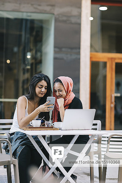 Zwei Freunde sitzen mit dem Handy in einem Straßencafé zusammen
