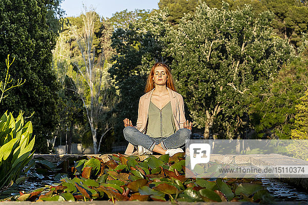 Junge rothaarige Frau meditiert in einem Park