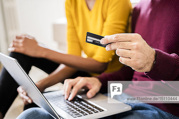 Nahaufnahme eines Paares beim Online-Einkauf zu Hause mit Laptop und Kreditkarte
