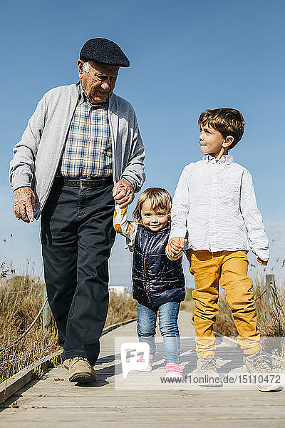 Großvater schlendert mit seinen Enkelkindern Hand in Hand auf der Promenade