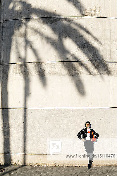 Glückliche junge Frau mit einer roten Hüfttasche  die auf einer Wand mit dem Schatten einer Palme ruht.