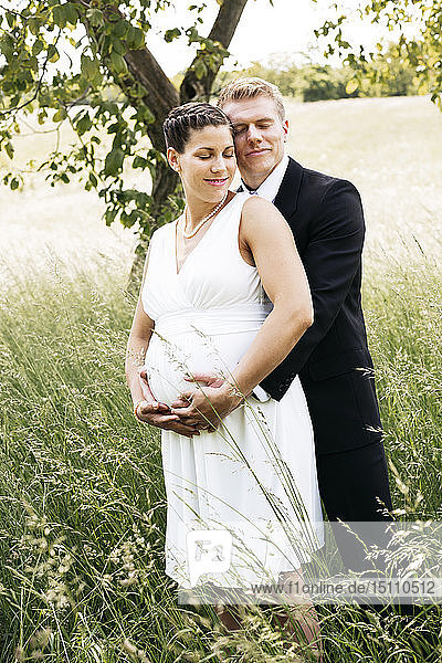 Pregnant bride with his husband holding baby belly on a meadow