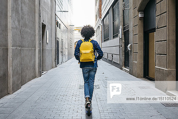 Rückenansicht eines jungen Mannes mit gelbem Rucksack auf einem E-Scooter in der Stadt  Barcelona  Spanien