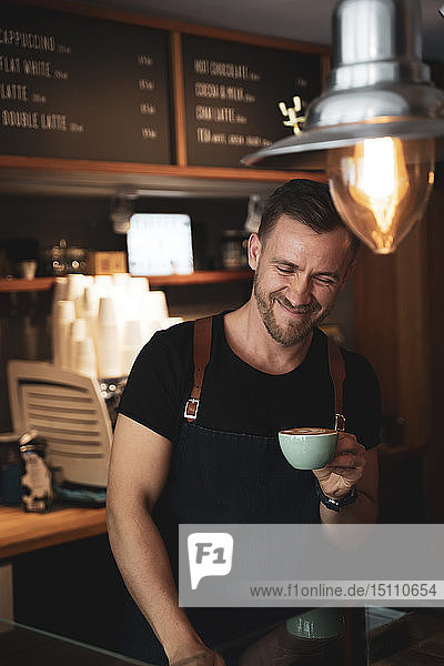 Smiling barista holding a coffee cup in coffee shop