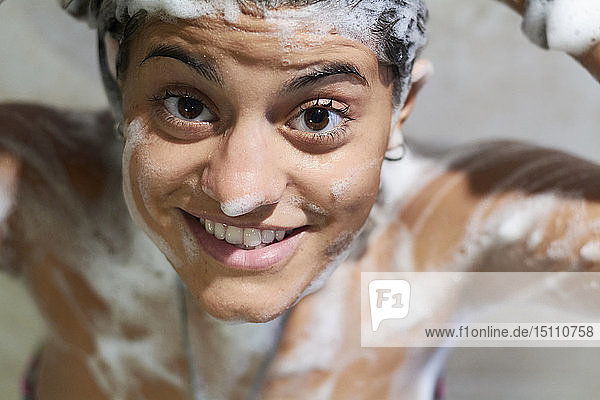 Lächelnde junge Frau  die mit Seife am Körper duscht und in die Kamera schaut