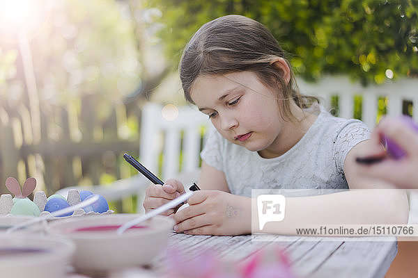Mädchen malt Osterei auf Gartentisch