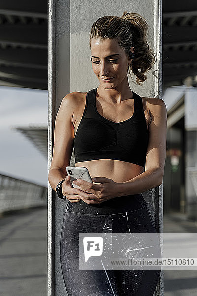 Sporty woman with headphones standing on bridge  listening music  using smartphone