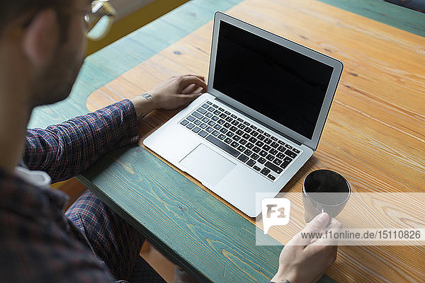 Pyjama tragender Mann sitzt mit Kaffeetasse vor dem Laptop
