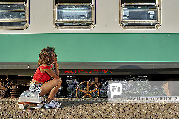 Frau mit Koffer auf dem Bahnhof sitzend