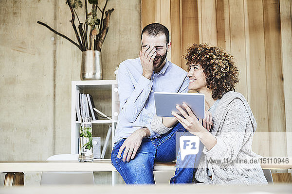 Happy man and woman sharing tablet in modern office
