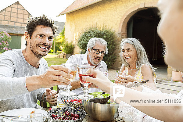 Fröhliche Familie beim gemeinsamen Essen im Garten  anstoßend