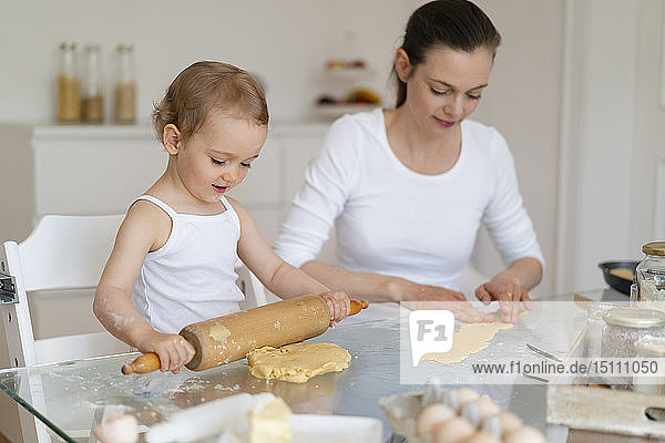 Mutter und kleine Tochter mit Teigrolle  die zu Hause in der Küche gemeinsam einen Kuchen backen