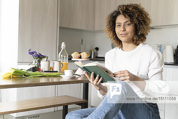 Woman sitting in kitchen reading book