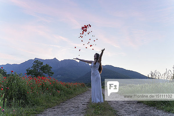 Elegante junge Frau wirft Mohnblütenblätter in die Landschaft  Garrotxa  Spanien