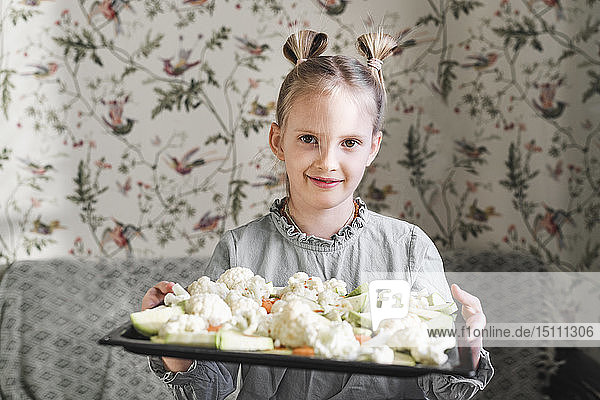 Portrait of blond girl with baking tray of raw vegetables