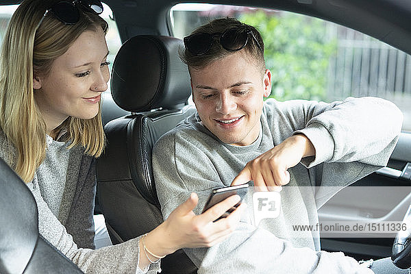 Smiling young couple in a car looking at cell phone