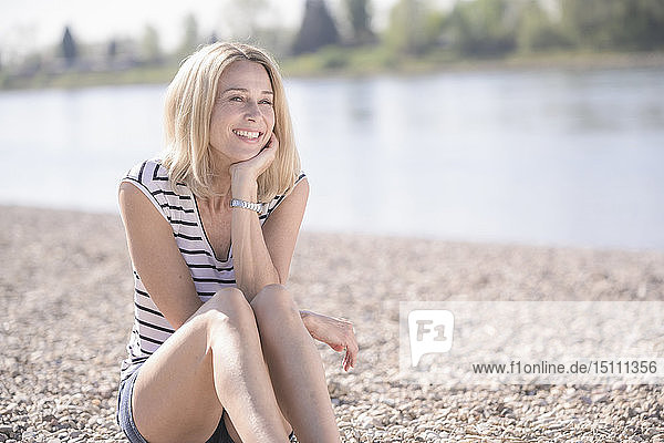 Lächelnde reife Frau sitzt am Flussufer