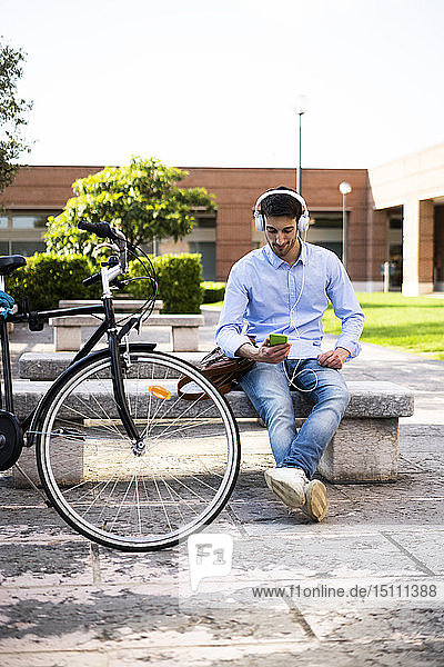 Junger Mann mit Fahrrad  der ein Smartphone benutzt und Musik hört