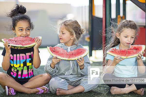 Three girls eating watermelons in kindergarten