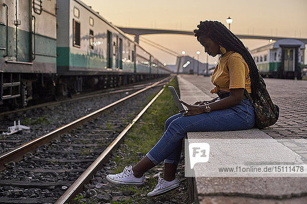 Junge Frau sitzt auf dem Bahnsteig im Bahnhof mit Laptop