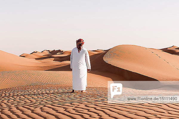 Beduine in Nationaltracht in der Wüste stehend  Rückansicht  Wahiba Sands  Oman