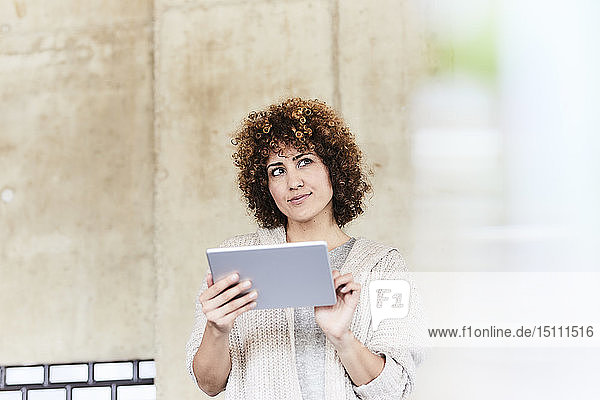 Lächelnde Frau mit Tablette an Betonwand