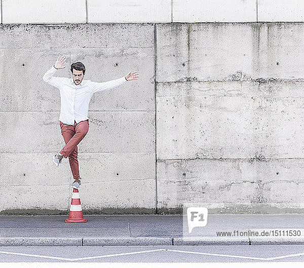 Junger Mann balanciert auf Verkehrskegel vor Betonmauer