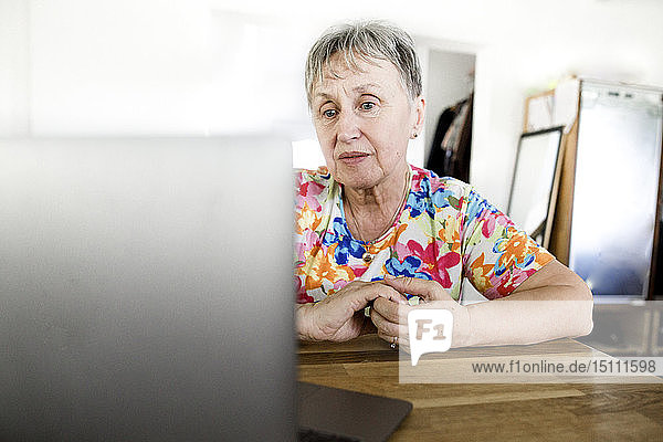 Ältere Frau sitzt zu Hause am Tisch mit Laptop