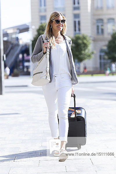 Young businesswoman looking at camera while walking with suitcase