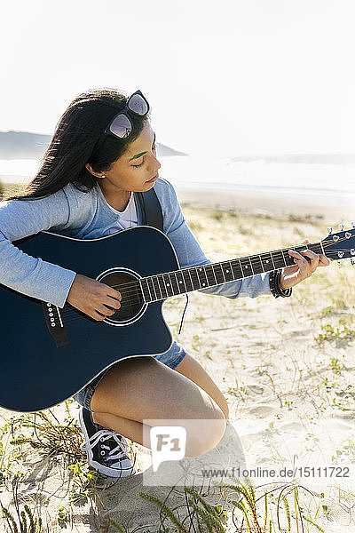 Junge Frau spielt Gitarre am Strand