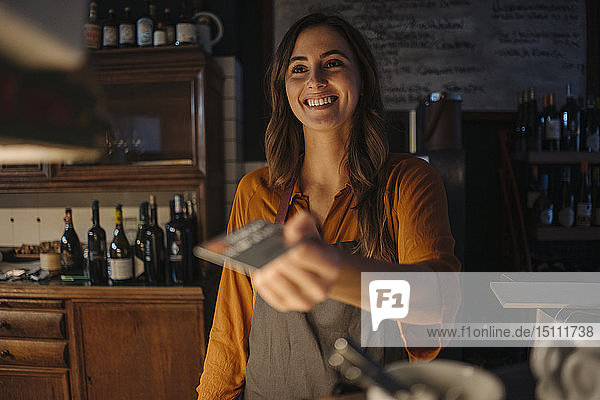 Smiling young woman at restaurant counter handing over credit card