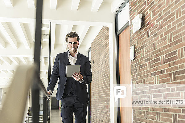 Junger Geschäftsmann steht auf Galerie in modernem Bürogebäude und benutzt digitales Tablet