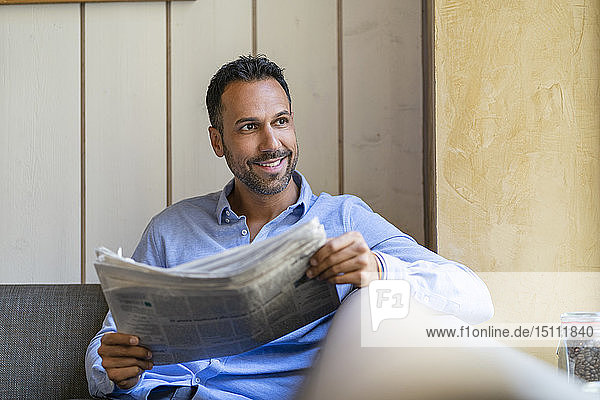 Lächelnder Geschäftsmann setzt sich hin und liest Zeitung