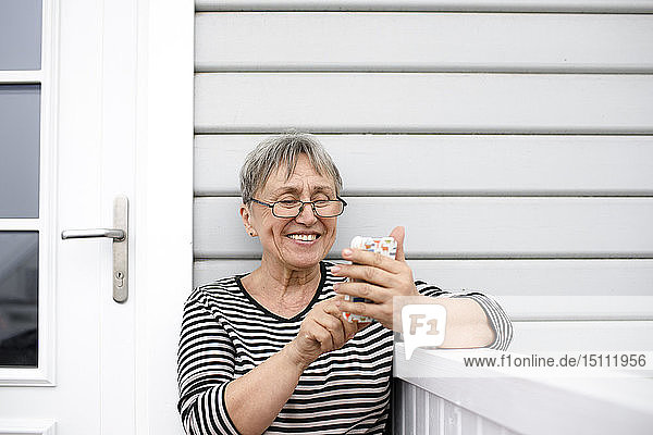 Glückliche ältere Frau benutzt Handy auf der Veranda ihres Hauses