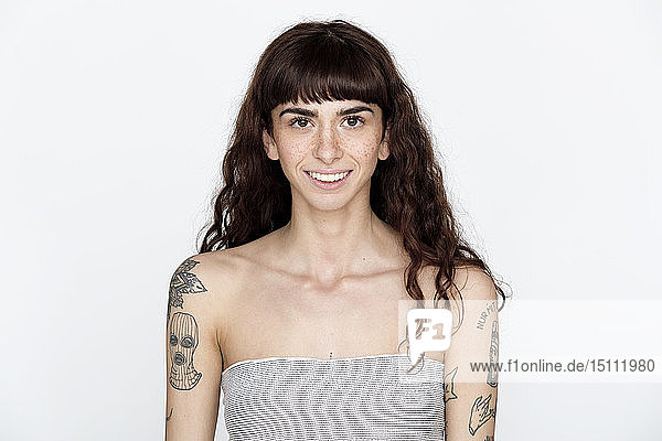 Portrait of smiling young woman with freckles and tattoos on her upper arms