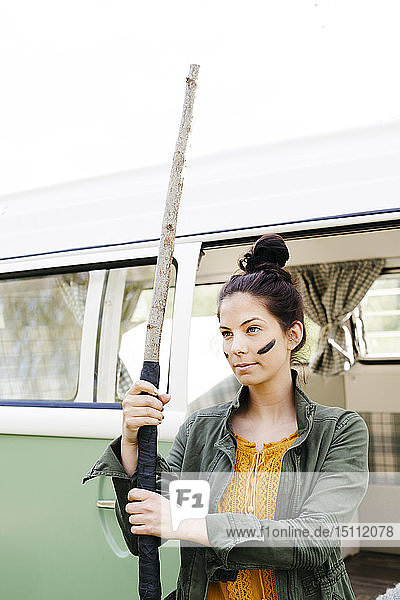 Young woman with spear and facepaint in front of her camper