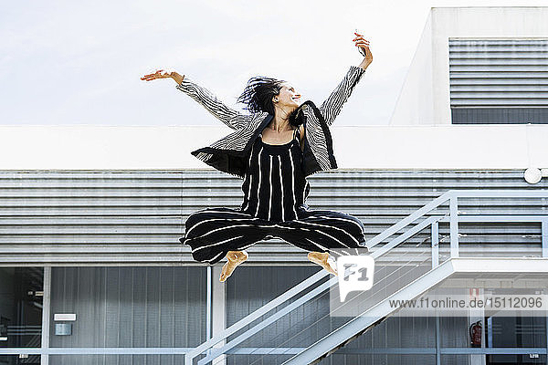 Balletttänzerin  die mit einem Smartphone springt und vor einem Bürogebäude einen Selfie macht