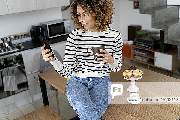 Frau sitzt zu Hause  benutzt Smartphone  isst Muffin