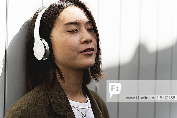 Relaxed young woman with closed eyes listening to music with headphones
