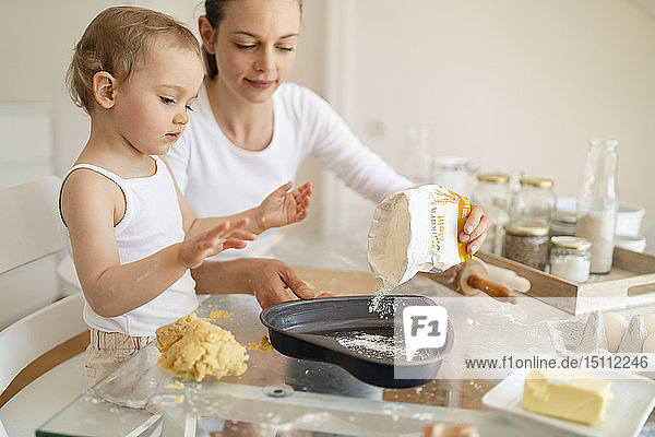 Mutter und kleine Tochter backen zu Hause in der Küche gemeinsam einen Kuchen