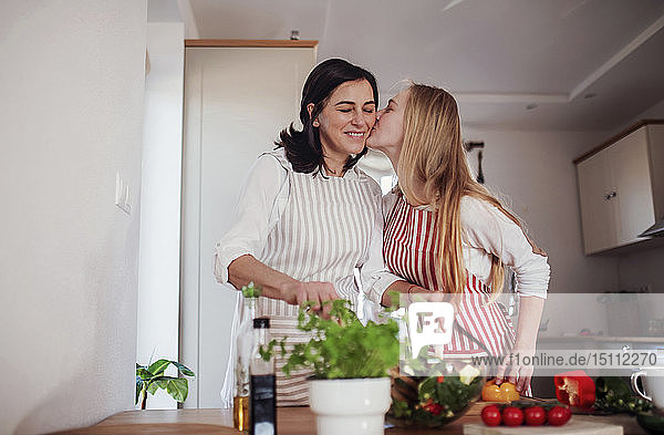 Tochter küsst Mutter  während sie in der Küche Gemüse schneidet