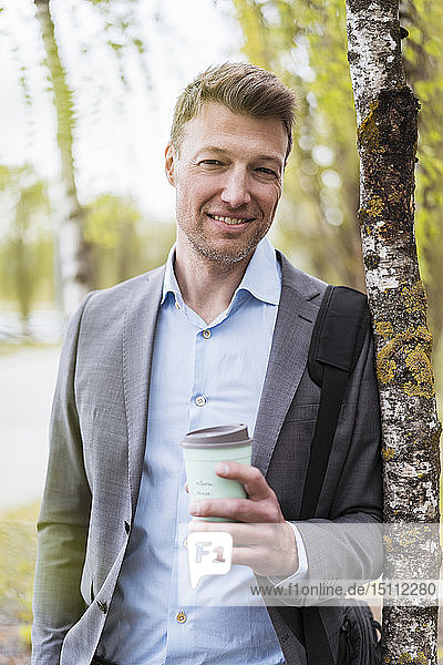 Smiling businessman with takeaway coffee in a park