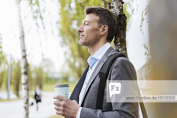 Entspannter Geschäftsmann mit Kaffee zum Mitnehmen in einem Park