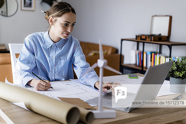Frau im Büro arbeitet an Plan und Laptop mit Windturbinenmodell auf dem Tisch